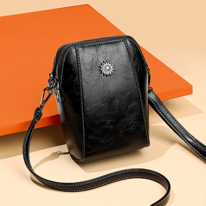 Sac en cuir noir posé sur un décor orange et beige, sangle déroulée au premier plan 6