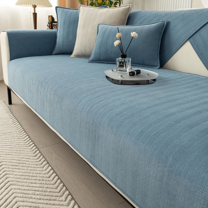 Housse de canapé bleue texturée en gros plan, avec coussins bleus et crème et un plateau de décoration sur l'assise. 3