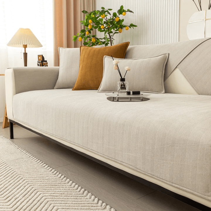 Housse beige clair à chevrons sur un canapé, accompagnée de coussins beige et moutarde, tapis à motifs en zigzag au sol. 2