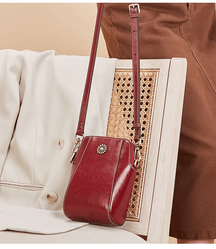 Sac en cuir rouge bordeaux suspendu par sa sangle réglable au dossier d'une chaise en cannage 5