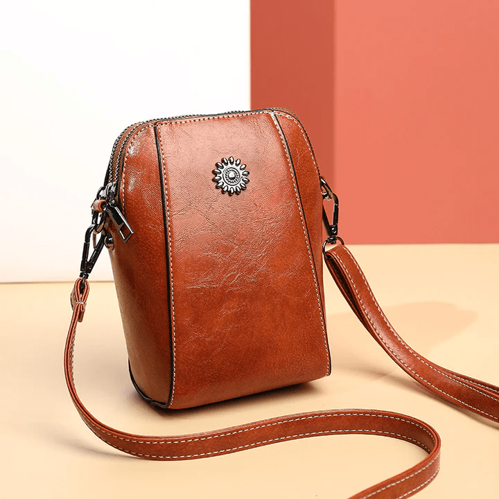 Petit sac vertical en cuir brun roux, posé en trois quarts avec sa longue sangle sur fond coloré 1