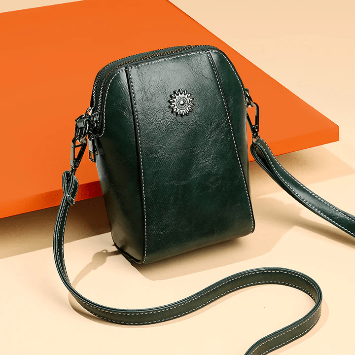 Sac en cuir vert foncé posé contre un panneau orange, avec sa sangle étalée devant 8