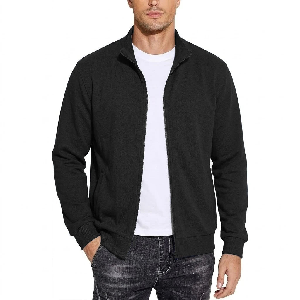 Homme portant la veste zippée noire ouverte sur un t-shirt blanc, col montant, poignets côtelés, une main dans la poche. 1