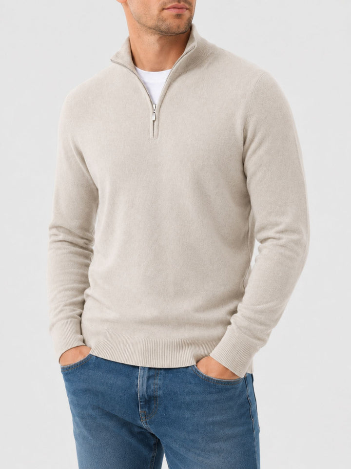 Homme portant le pull beige clair à col zippé avec un jean bleu, vue de face, une main dans la poche. 1