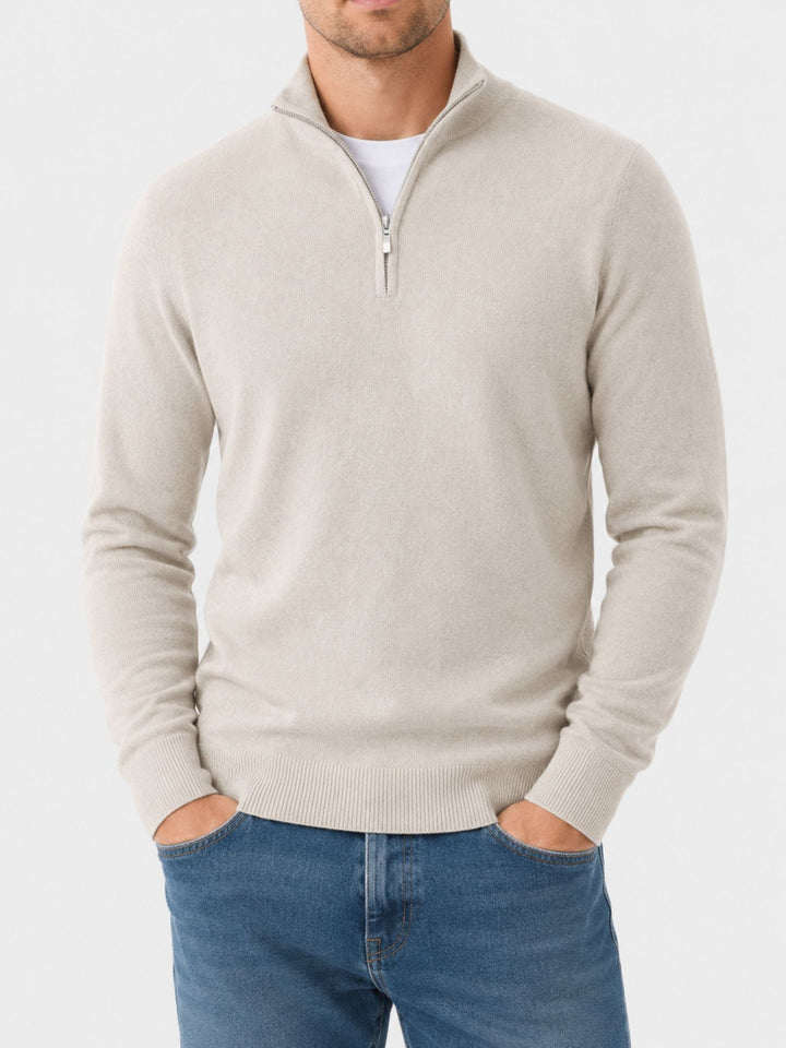 Homme debout face à l'objectif, mains dans les poches du jean, portant le pull beige à col zippé et t-shirt blanc. 10