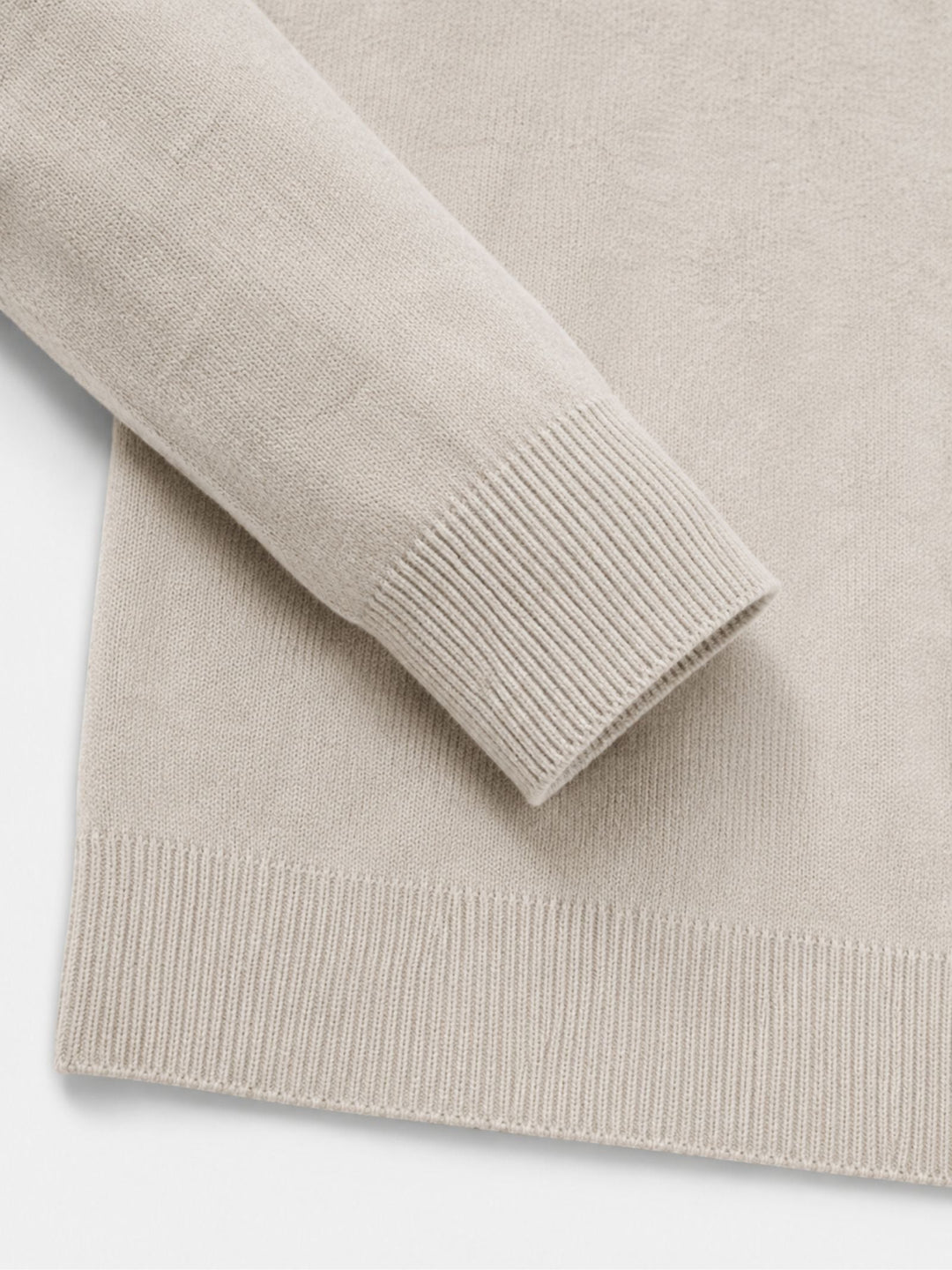 Détail du poignet et de l'ourlet côtelés du pull beige, manche repliée sur le corps du vêtement. 15