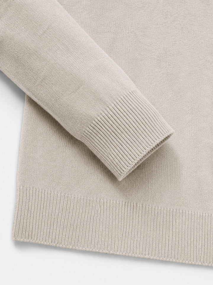 Détail du poignet et de l'ourlet côtelés du pull beige, manche repliée sur le corps du vêtement. 15