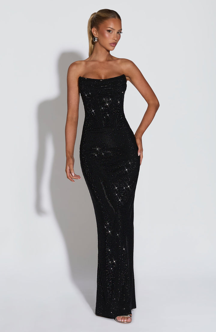 Robe noire à strass portée de face par un mannequin à queue-de-cheval haute, une main sur la hanche, silhouette fourreau jusqu'au sol. 22