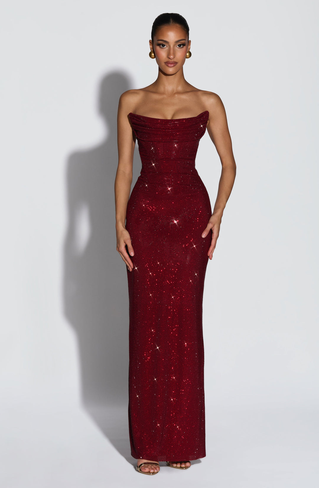 Vue de face de la robe longue bustier rouge bordeaux couverte de strass, portée par une mannequin, corsage drapé et jupe ajustée 1