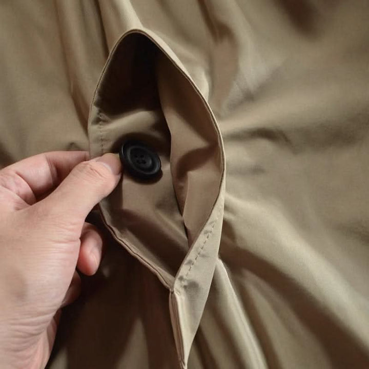 Gros plan sur la poche latérale du manteau beige, tenue ouverte par une main, avec un bouton noir à l'intérieur. 8