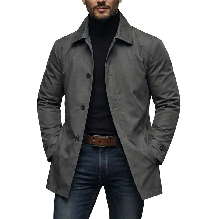 Homme portant le manteau gris anthracite sur un col roulé noir et un jean, mains dans les poches, sur fond blanc. 1