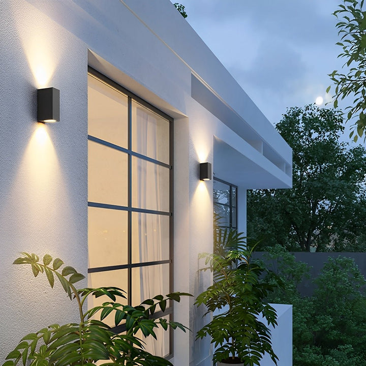 Deux appliques rectangulaires noires à double faisceau sur la façade blanche d'une maison, entourées de plantes 4