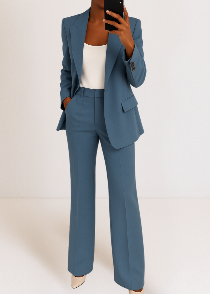 Femme en selfie miroir portant l'ensemble bleu acier, blazer à revers cranté ouvert sur un haut blanc, pantalon évasé à pli. 1