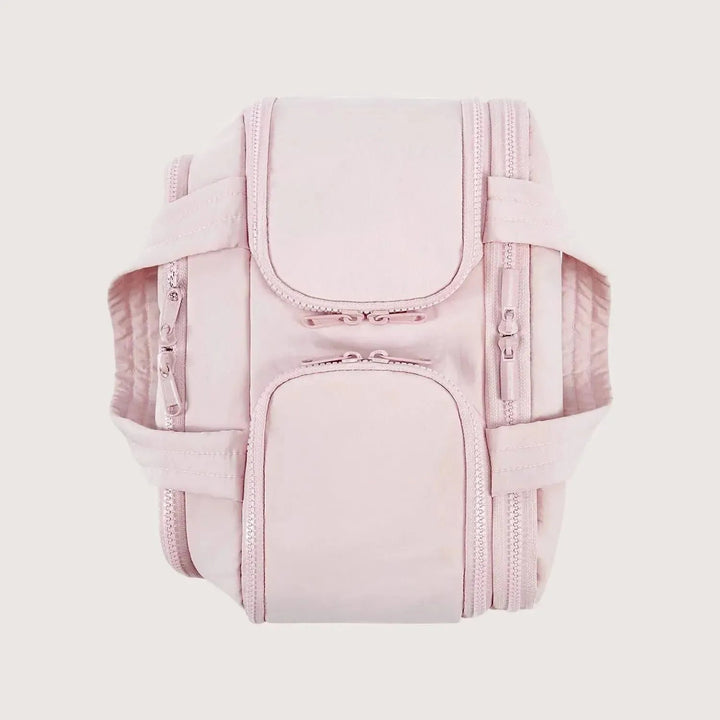 Trousse rose vue de dessus, anses rabattues sur les côtés et plusieurs volets zippés fermés sur le dessus. 11