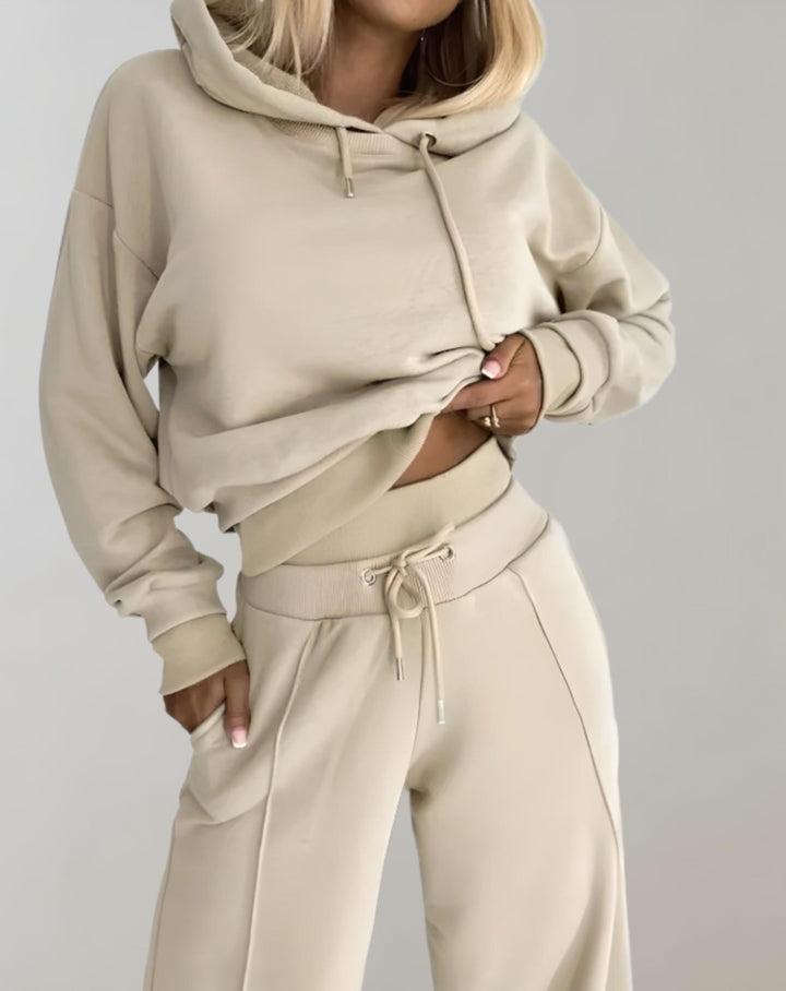 Gros plan sur l'ensemble beige, capuche, cordon de serrage et taille ceinturée du pantalon, une main dans la poche. 6