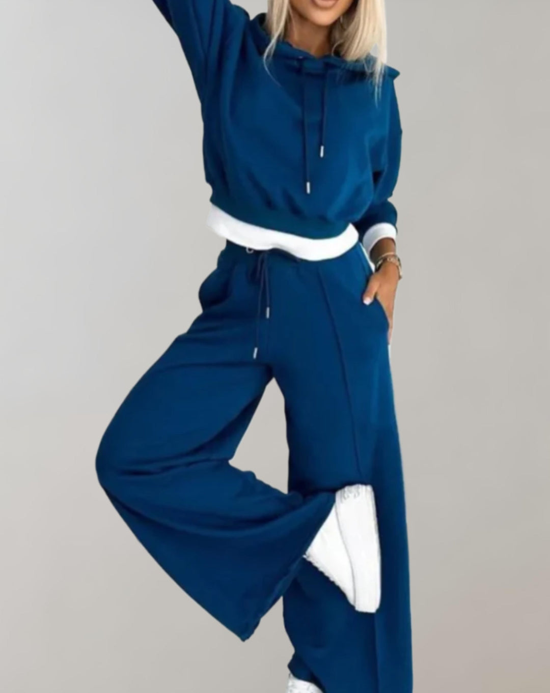 Ensemble bleu pétrole porté en mouvement, une jambe levée, avec sweat court à capuche et pantalon large, baskets blanches. 4