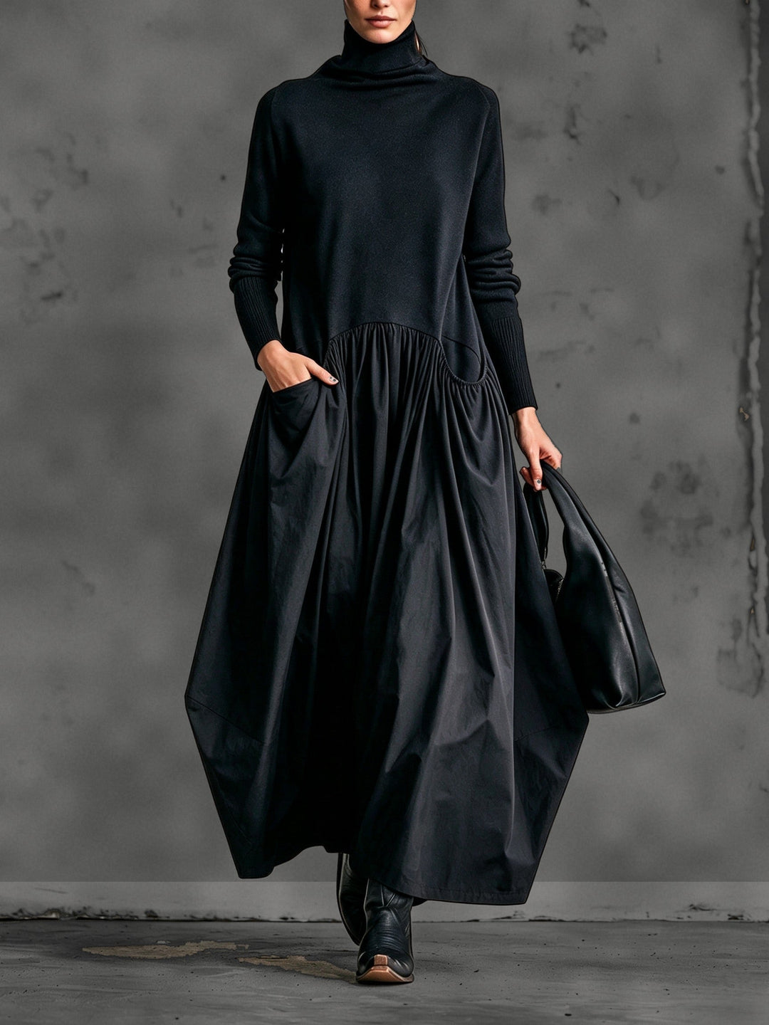 Vue de face de la robe noire portée par un mannequin, main dans la poche, sac noir 1