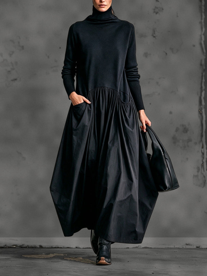 Vue de face de la robe noire portée par un mannequin, main dans la poche, sac noir 1