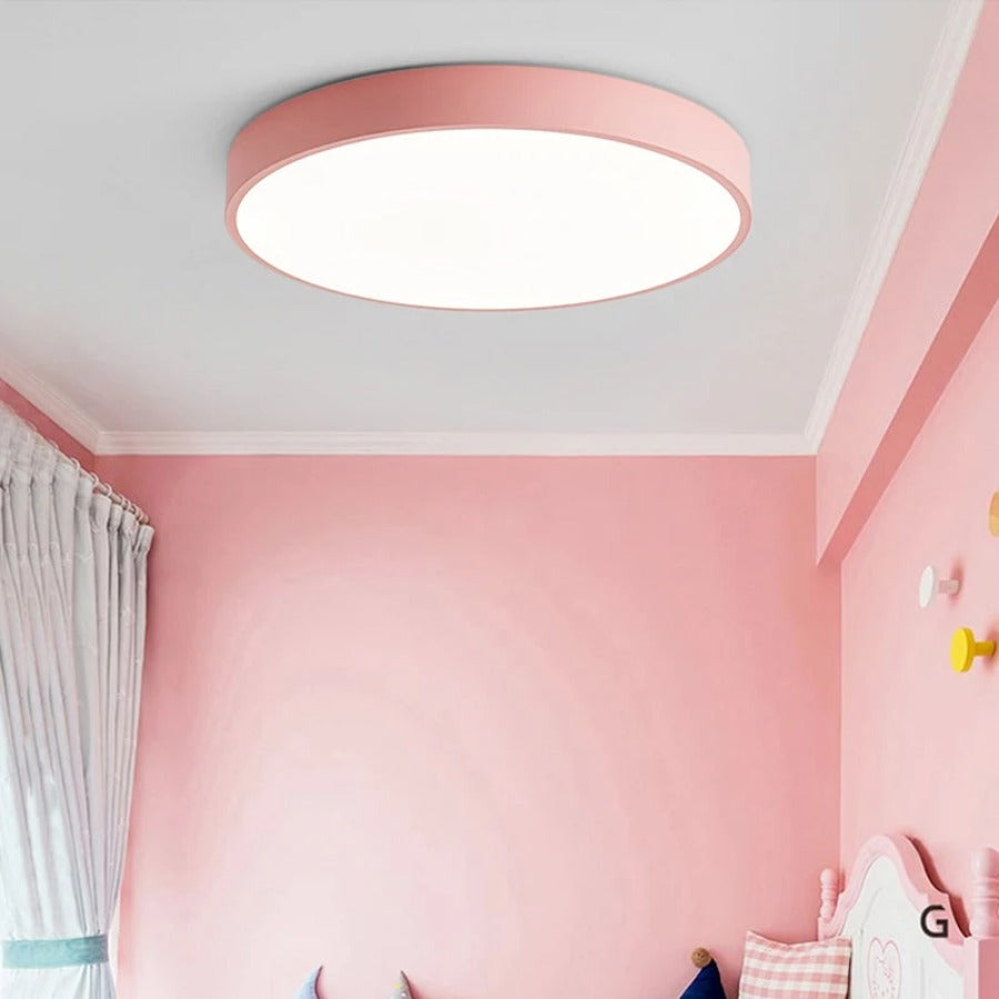 Plafonnier rond rose posé au plafond d'une chambre d'enfant aux murs roses, avec patères colorées et lit. 5