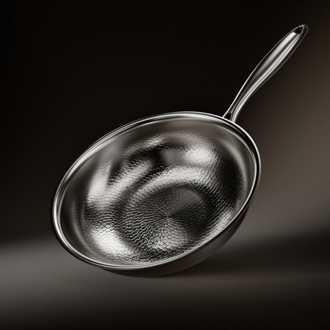 Wok incliné sur fond sombre, intérieur martelé à motif d'écailles, long manche métallique brillant et bord poli. 1
