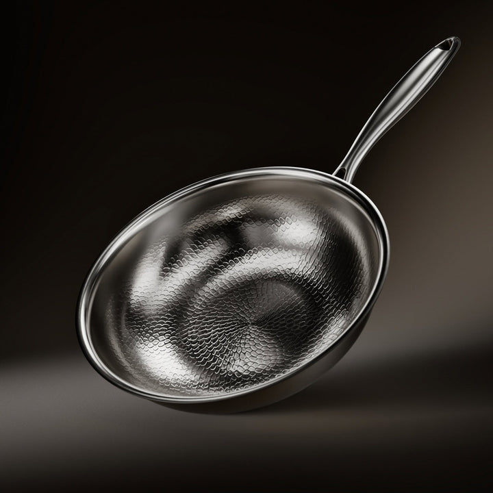 Wok incliné sur fond sombre, intérieur martelé à motif d'écailles, long manche métallique brillant et bord poli. 1