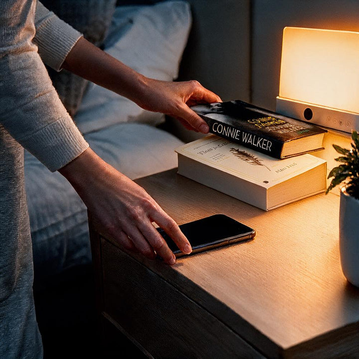 Lampe allumée sur une table de chevet, une main posant des livres près d'un téléphone 10