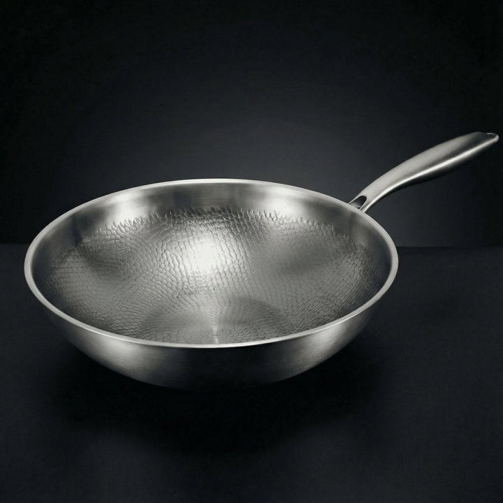 Wok en métal brossé vu de trois quarts sur fond sombre, intérieur martelé en écailles et long manche. 1