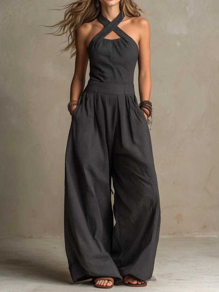 Femme portant la combinaison dans sa version gris anthracite finement rayée, mains dans les poches, avec bracelets et sandales marron. 1