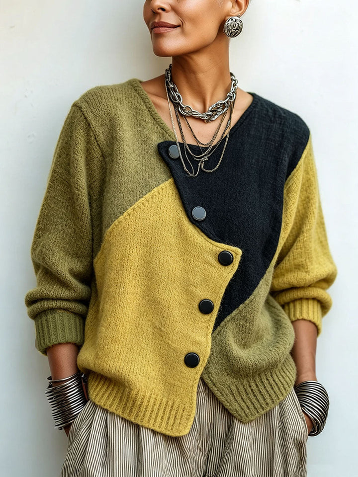 Plan rapproché du buste d'une femme portant le pull colorblock olive, moutarde et noir, boutons asymétriques et colliers argentés, fond clair. 1