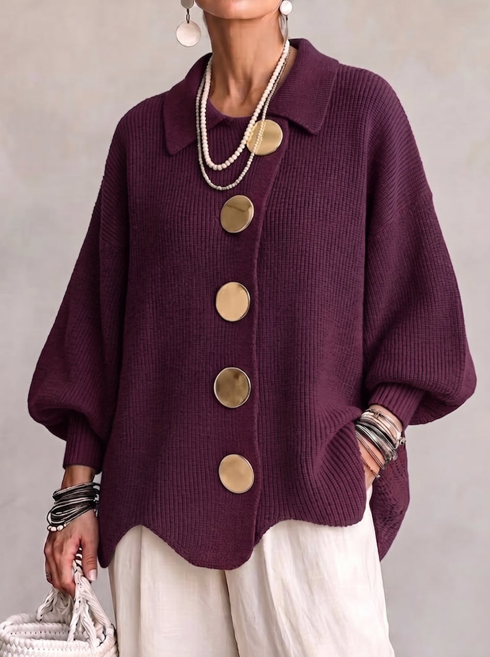 Vue de face du cardigan prune en maille côtelée, porté avec un pantalon blanc, grands boutons dorés et manches bouffantes. 2