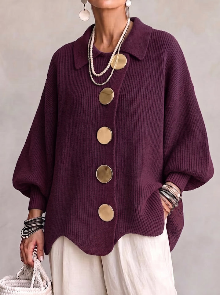 Vue de face du cardigan prune en maille côtelée, porté avec un pantalon blanc, grands boutons dorés et manches bouffantes. 2
