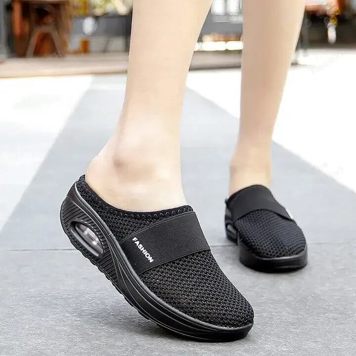 Mules noires en maille portées en marchant sur un trottoir gris, semelle compensée à coussin d'air visible 3