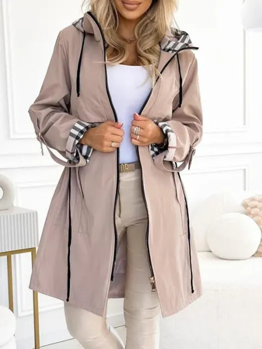 Veste beige rosé portée ouverte avec un pantalon beige, capuche à cordons, poignets retroussés laissant voir la doublure à carreaux. 2