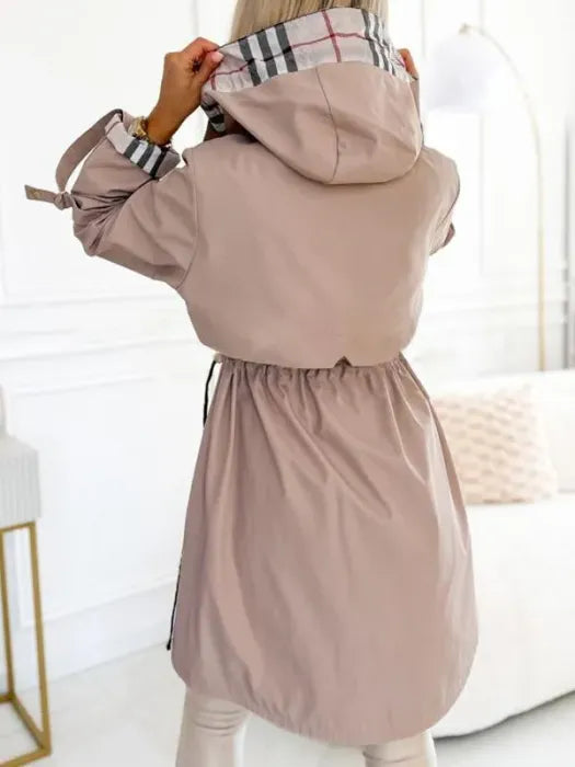 Vue de dos de la veste beige rosé, capuche doublée à carreaux relevée par la mannequin, taille resserrée par un cordon. 3