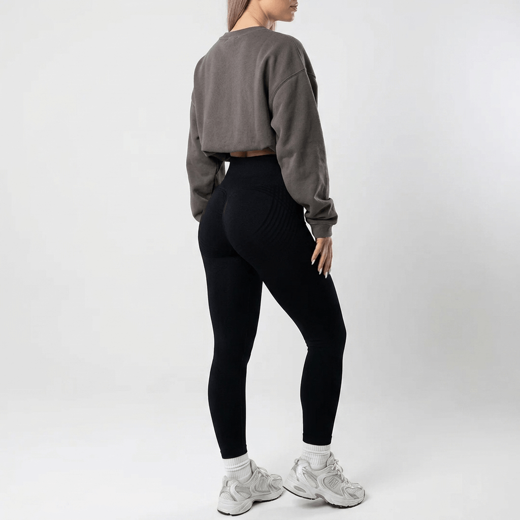 Legging noir taille haute porté de dos avec un sweat gris oversize court, sur fond blanc et baskets claires. 25