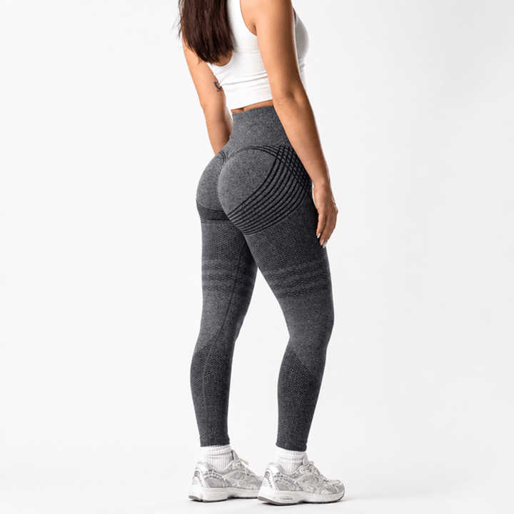 Legging gris anthracite taille haute vu de trois quarts dos sur fond blanc, avec rayures courbes sur les fesses et baskets grises. 23