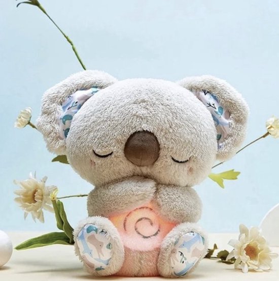 Peluche koala aux yeux fermés et aux oreilles doublées de tissu fleuri, ventre orangé lumineux, entouré de fleurs blanches. 1