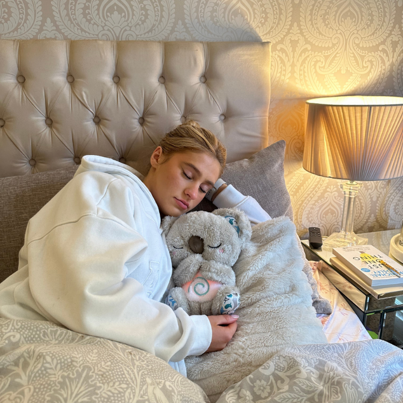 Jeune femme endormie dans un lit, un koala en peluche à la spirale lumineuse contre elle, près d'une lampe. 14