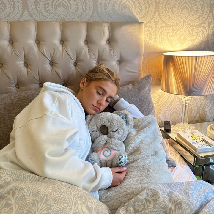 Jeune femme endormie dans un lit, un koala en peluche à la spirale lumineuse contre elle, près d'une lampe. 14