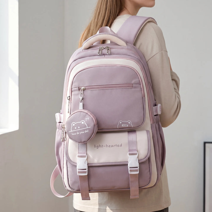 Sac à dos mauve et crème porté sur le dos par une jeune femme, vu de profil, avec sa petite pochette ronde suspendue. 1
