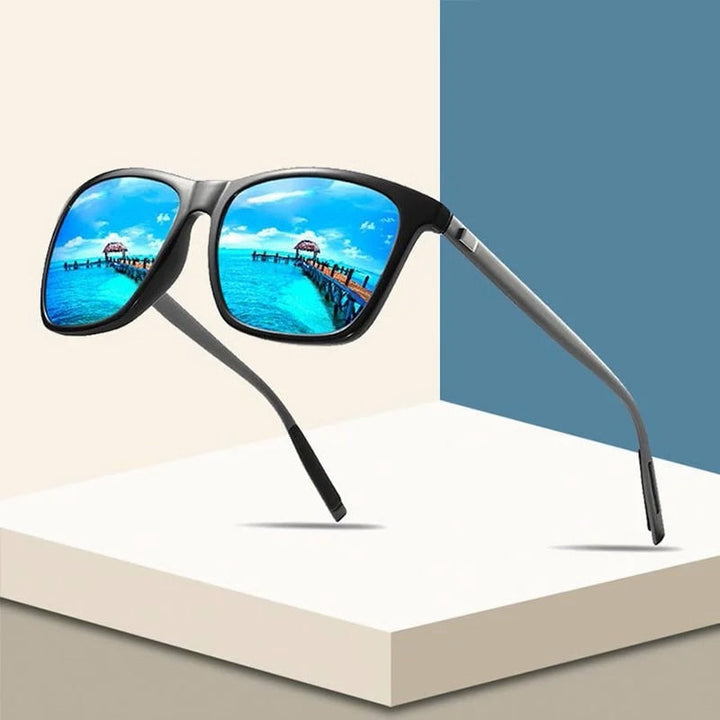 Monture noire aux verres miroir bleus reflétant un ponton sur mer turquoise, posée sur des blocs géométriques 1