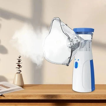 Nébuliseur blanc et bleu avec masque transparent posé sur une table en bois, diffusant un nuage de vapeur dans une pièce lumineuse. 1