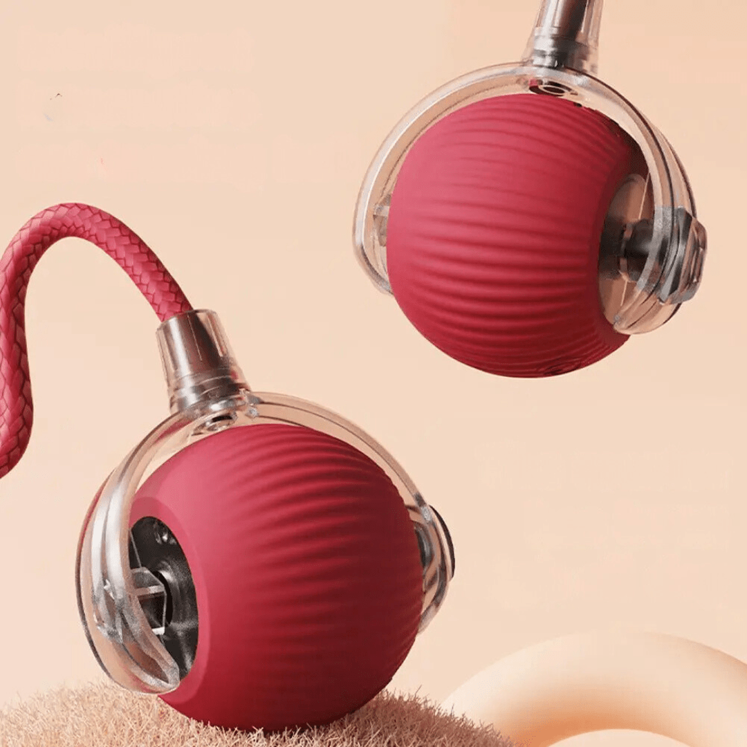 Gros plan sur deux balles rouges nervurées, coque transparente et mécanisme visible, l'une avec sa corde tressée, sur fond pêche. 15
