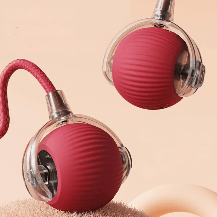 Gros plan sur deux balles rouges nervurées, coque transparente et mécanisme visible, l'une avec sa corde tressée, sur fond pêche. 15