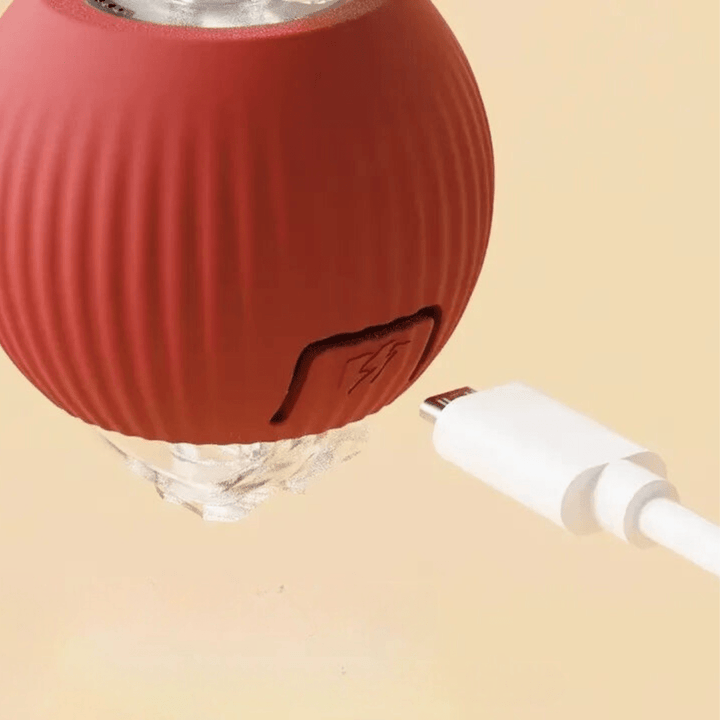 Gros plan sur la balle rouge nervurée et son câble USB blanc prêt à se brancher dans le port de recharge. 8