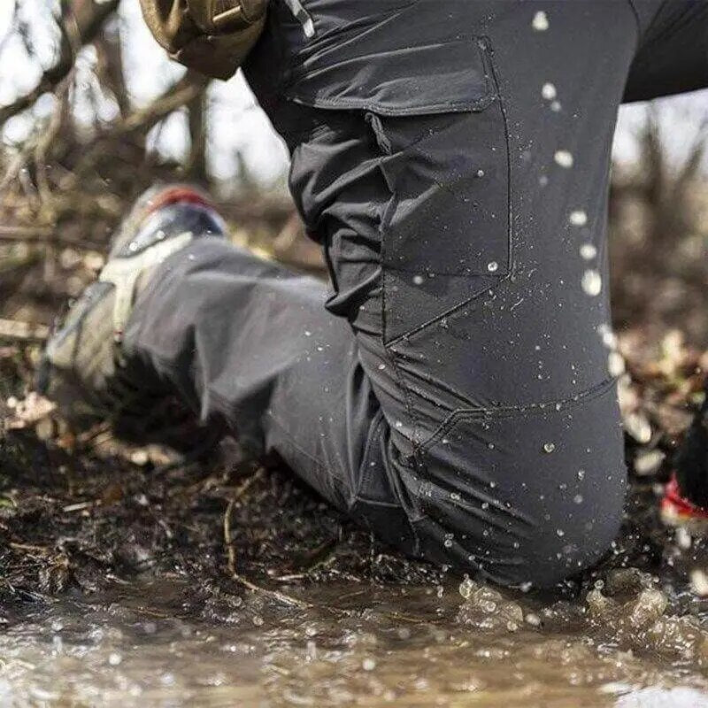 Pantalon gris foncé porté à genoux dans une flaque boueuse, avec des gouttes d'eau projetées sur la poche cargo. 3