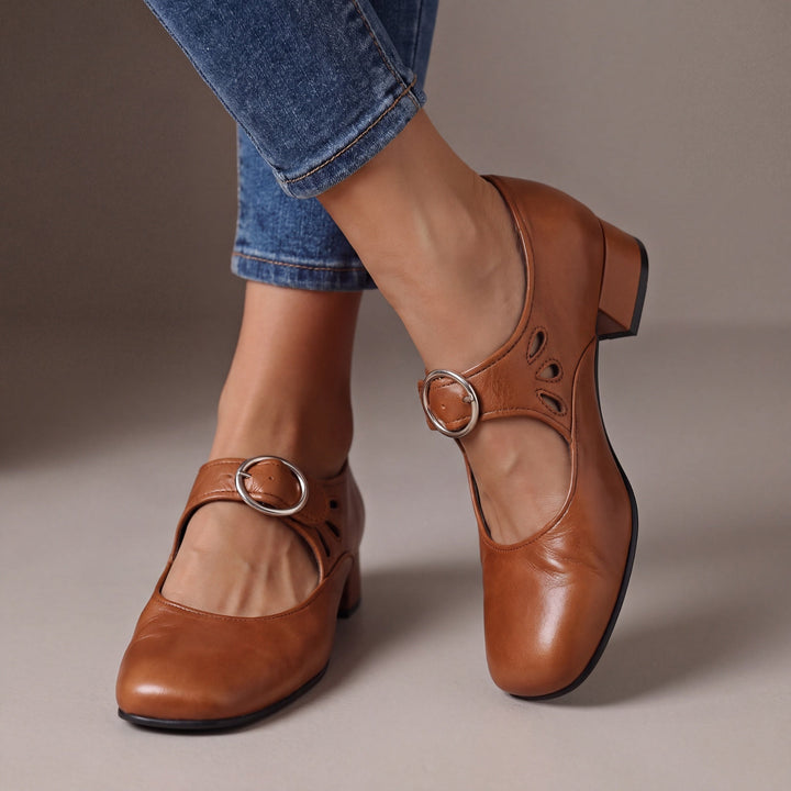 Escarpins marron caramel à talon bloc et boucle ronde argentée, portés avec un jean, avec découpes en goutte sur le côté. 3