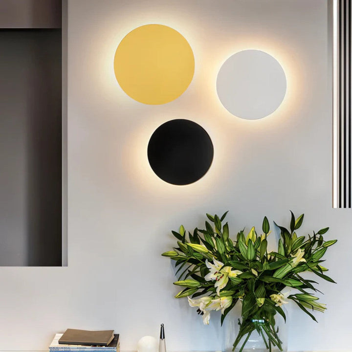 Trois appliques rondes doré, blanc et noir groupées sur un mur au-dessus d'un bouquet de lys 4