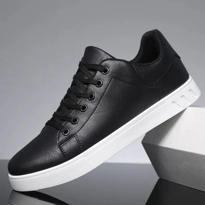 Même modèle de baskets basses en version noire, lacets noirs et semelle blanche, présentées sur un bloc gris clair. 2
