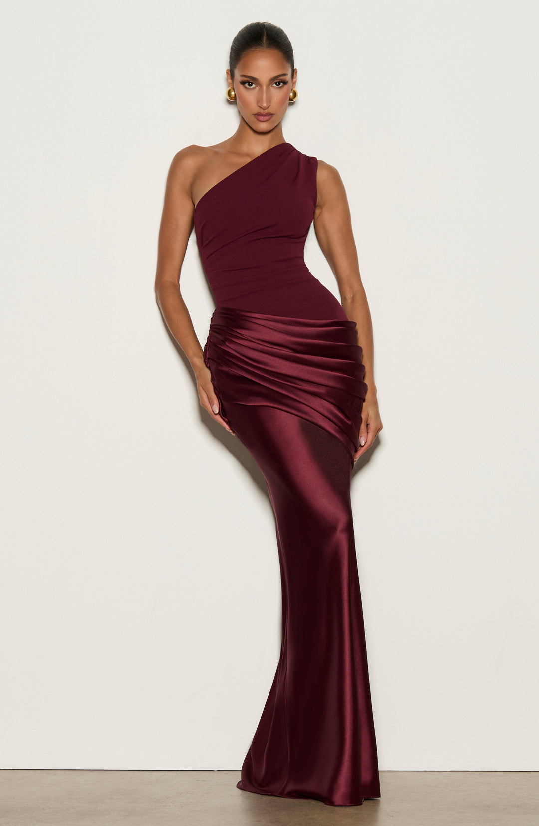 Gros plan sur le buste et le drapé de la robe prune, épaule unique et plis en satin brillant. 16